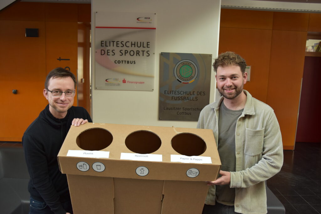 Schulsekretär Christian Schneider (l.) und Netzwerkleiter Jona Peters besiegelten die Zusammenarbeit mit der Übergabe von zwei Trio-Abfalleimern. Foto: Thomas Juschus